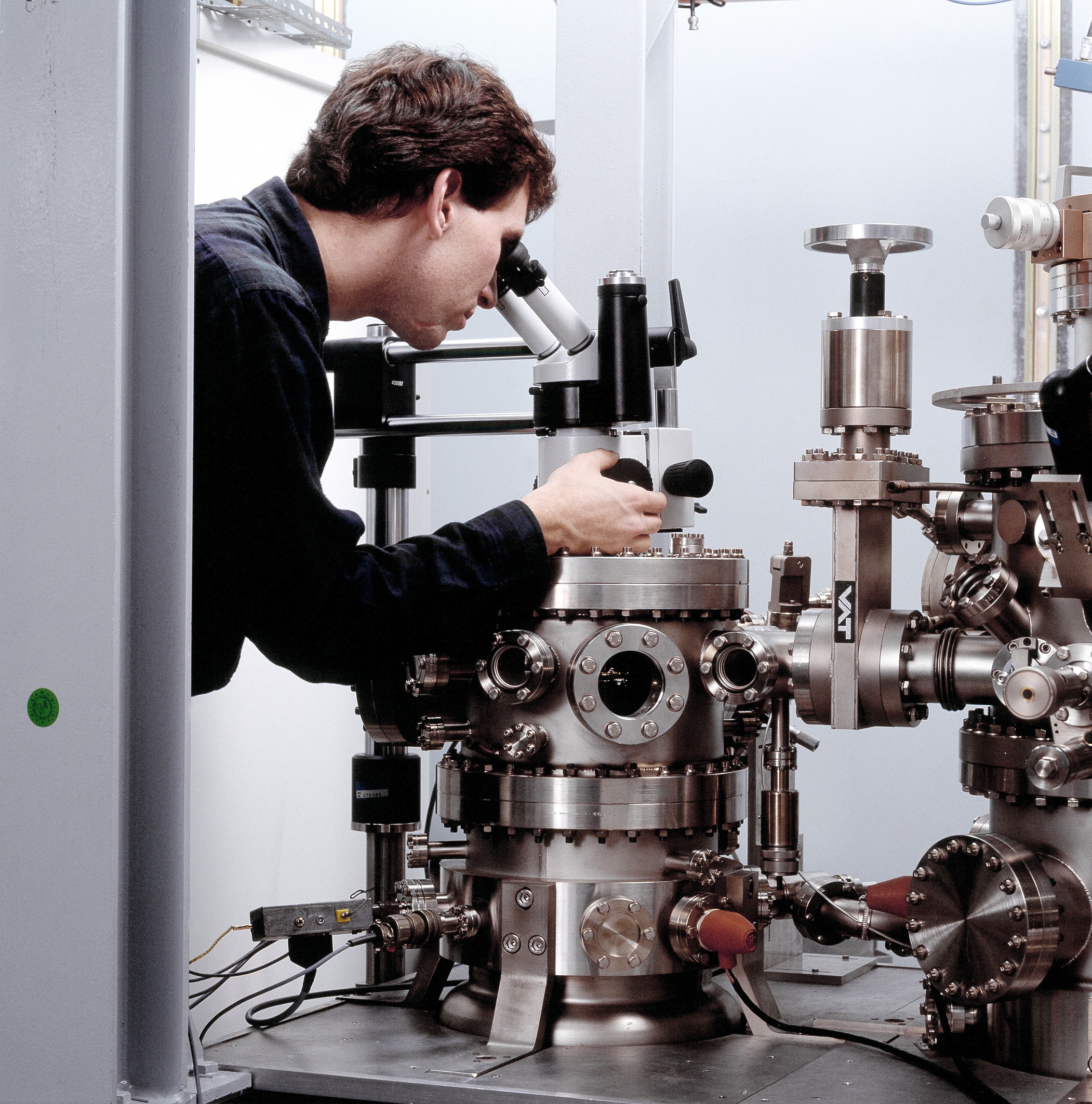Mitarbeiter schaut in ein Mikroskop an einem aus Edelstahl gebauten Instrument